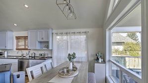 Una cocina moderna con armarios blancos, una mesa de comedor con sillas, un horno empotrado y un amplio ventanal con vistas al exterior.