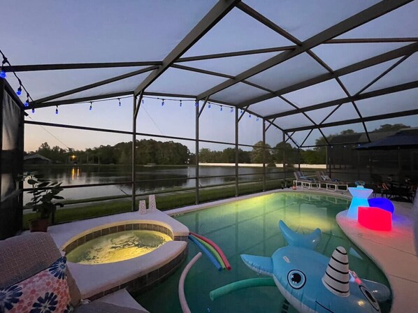 Una piscina exterior con hidromasaje, juguetes inflables y tumbonas.