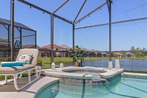 Zona de piscina con un jacuzzi, sillas de descanso y vistas a un lago y casas al fondo.