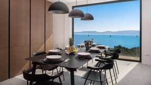 Un espace de restauration moderne doté d’une grande fenêtre donnant sur un plan d’eau, d’une table dressée pour un repas et d’un éclairage suspendu.