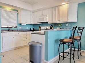 A kitchen with white cabinets, a microwave, a trash can, and two bar stools.
