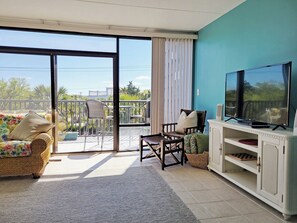 Una habitación con balcón, televisor, sofá y escritorio.