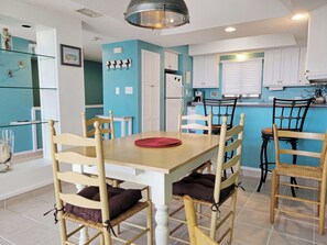 Un comedor con mesa y sillas de madera, una cocina al fondo y una pared azul de acento.