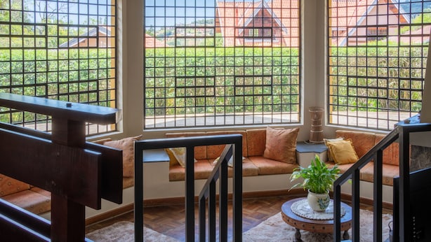 A cozy seating area with a sofa and a small table, a staircase with a railing, and a view through a window with a grid pattern. - Casa Mantiqueira - Campos do Jordão (Campos do Jordão)