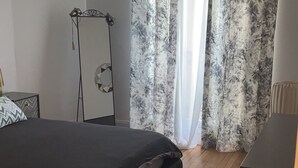 Une chambre à coucher avec un lit, un plancher en bois, un grand miroir et des rideaux à motifs floraux.