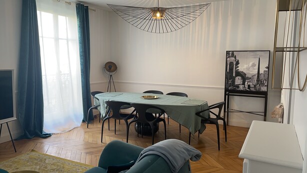 Un coin repas avec une table dressée pour quatre personnes, un ventilateur de plafond et un tableau encadré au mur.