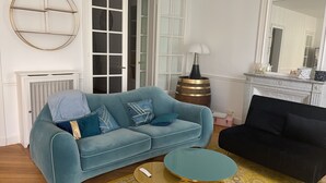 Un salon avec un canapé bleu clair, un canapé noir, une table basse ronde, une cheminée et un grand miroir.
