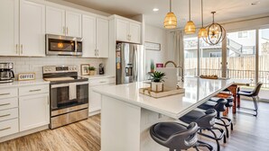 A modern kitchen with white cabinetry, stainless steel appliances, and a central island with bar stools. - Bright Colorado Springs Home, 10 Mi to Dtwn! (Colorado Springs)