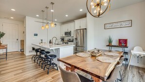 A modern kitchen with white cabinets, stainless steel appliances, and a wooden dining table with bar stools. - Bright Colorado Springs Home, 10 Mi to Dtwn! (Colorado Springs)