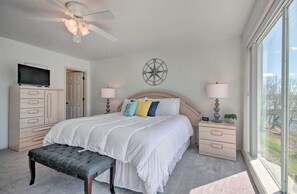 Une chambre à coucher comprenant un lit, des tables de chevet, un téléviseur, un ventilateur de plafond, une décoration murale représentant une boussole et une fenêtre avec vue.