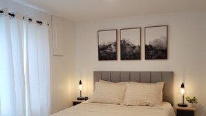 A bedroom with a large bed, two bedside tables with lamps, a ceiling light, and three framed pictures on the wall.