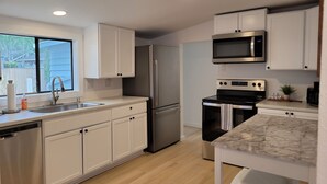 A modern kitchen with white cabinets, stainless steel appliances, a marble countertop, and a window providing natural light.