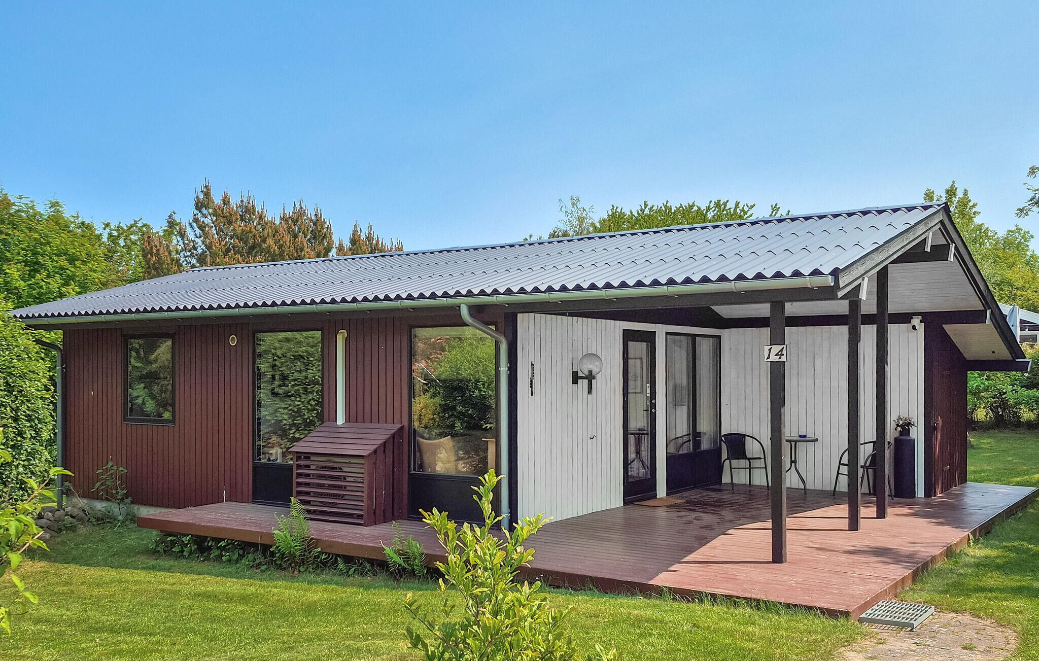 Eine kleine, eingeschossige Holzhütte mit einer Veranda und einer Terrasse.