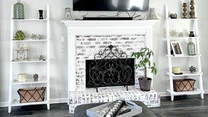 Un salon doté d’une cheminée, d’un téléviseur et de deux étagères blanches ornées d’objets décoratifs.