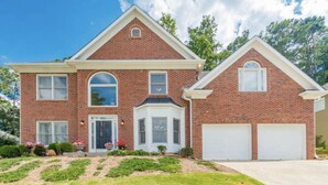 Une maison à deux étages, construite en briques, avec une entrée centrale, un garage et une pelouse bien entretenue.