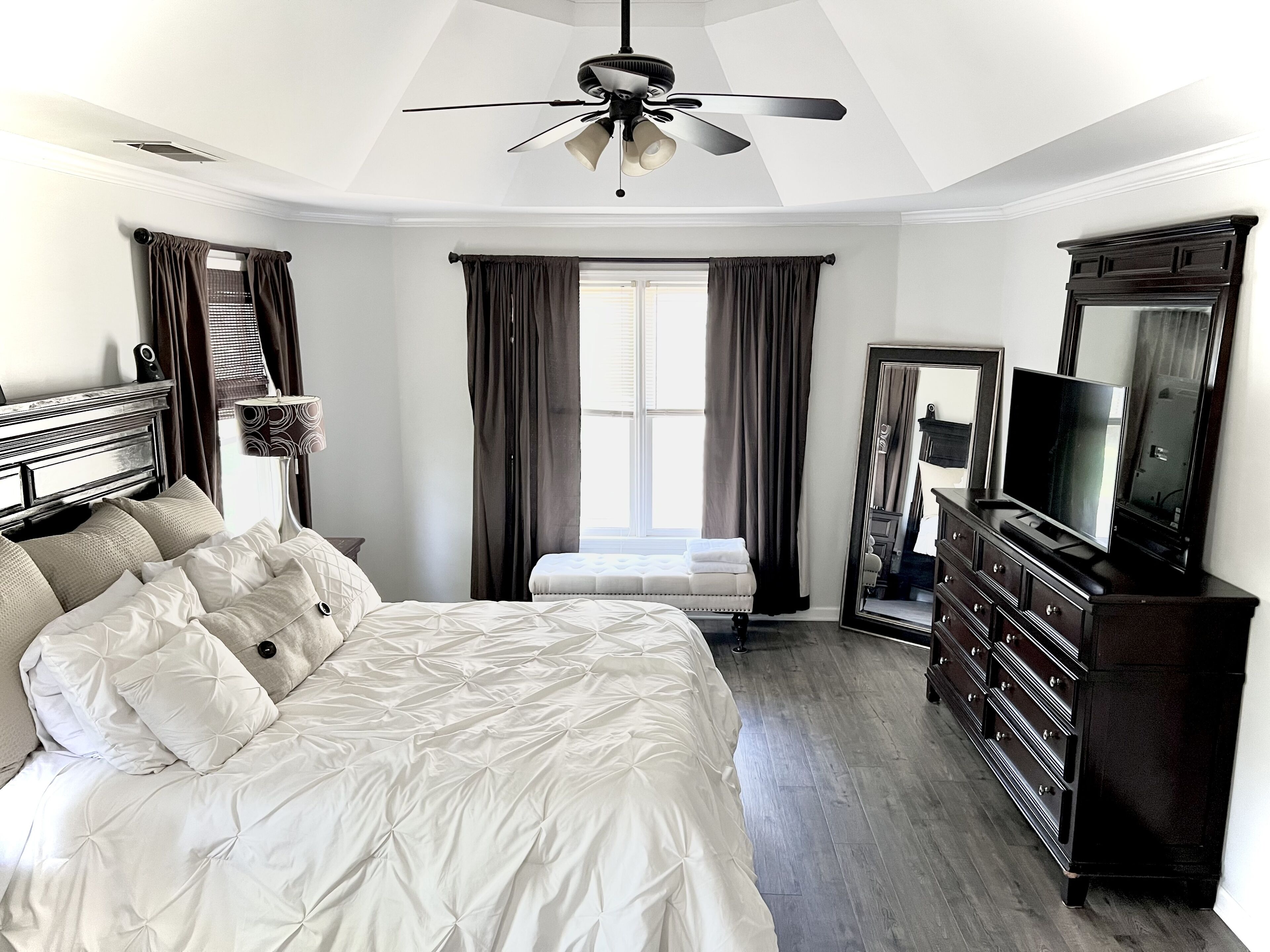 Une chambre à coucher comprenant un lit, une commode, un téléviseur et un ventilateur de plafond.