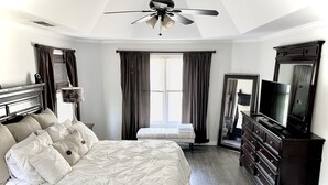 Une chambre à coucher comprenant un lit, une commode, un téléviseur et un ventilateur de plafond.