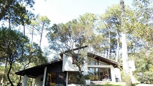 A modern house with a large glass front and a covered porch, surrounded by trees. - Villa ' L'échappée Belle' (SEIGNOSSE)
