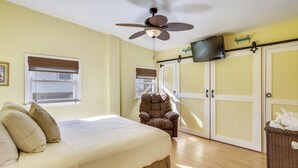 A bedroom with a bed, a chair, a ceiling fan, a television, and a wardrobe.