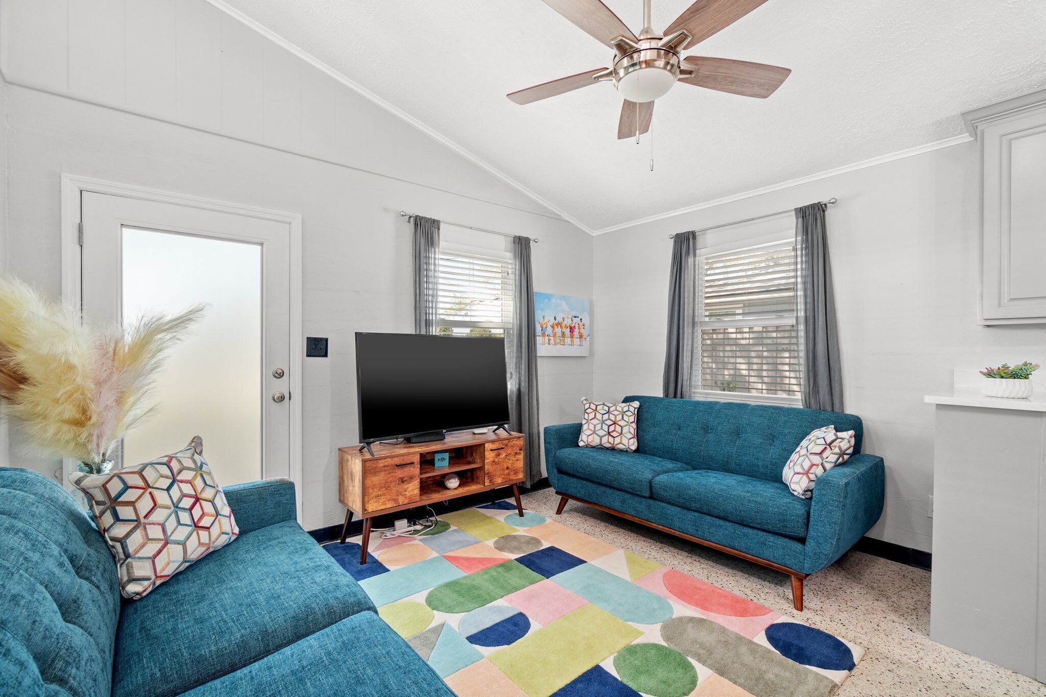 A living room with a blue sofa, a television on a wooden stand, and a ceiling fan.