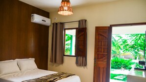 A bedroom with a bed, an air conditioning unit, a window with curtains, and a view of greenery outside. - Pousada Recanto Caiçara (São Miguel dos Milagres)