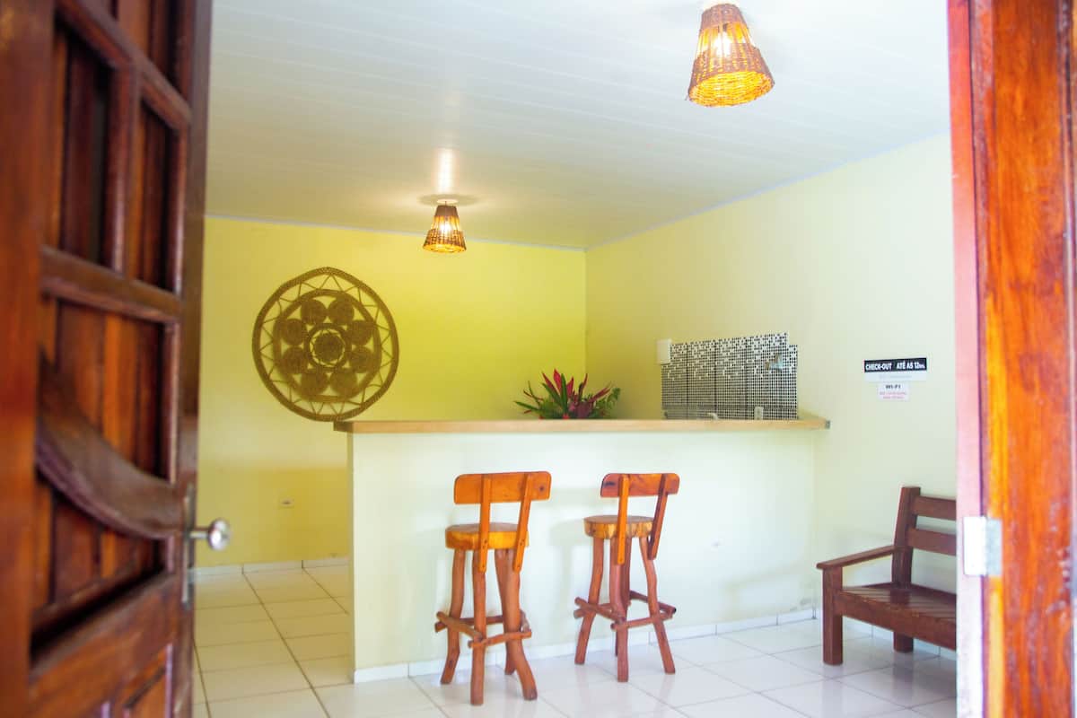 Una habitación con una puerta de madera, un mostrador de recepción con dos taburetes de bar de madera, un adorno en la pared y una lámpara colgante.