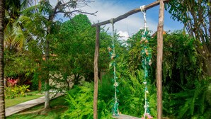 A wooden swing set with decorative elements in a lush garden. - Pousada Recanto Caiçara (São Miguel dos Milagres)
