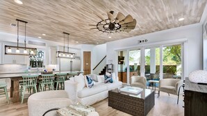 Un vaste espace de vie doté d’un plafond en bois, d’un canapé blanc et d’un coin repas avec des chaises vertes.