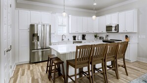 Una cocina moderna con armarios blancos, electrodomésticos de acero inoxidable y sillas de madera.