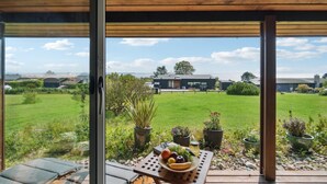 Un patio techado con una mesa dispuesta con frutas y verduras, con vistas a una zona ajardinada y un edificio de diseño moderno.