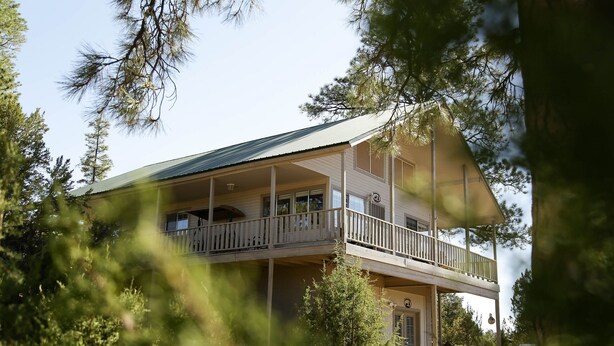 Una casa de dues plantes amb un balcó al pis superior, envoltada d'arbres.