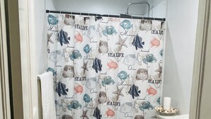 A bathroom with a white toilet, a blue bath mat, and a shower curtain with a marine life pattern.