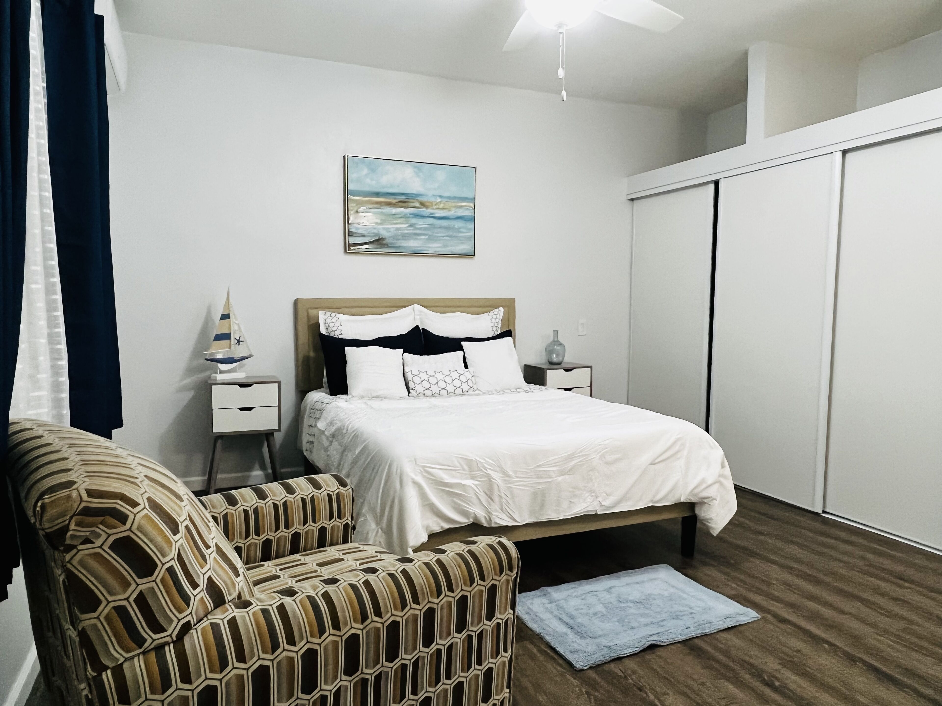 A bedroom with a bed, a nightstand, a chair, a painting, and a wardrobe.