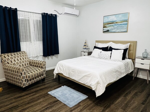 A bedroom with a bed, a chair, a nightstand, a wall-mounted air conditioner, a window with curtains, and a painting. - Adorable Private Room with partial Sea View (Sentry Hill)