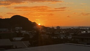 A sunset over a coastal town with buildings and a hill in the background.