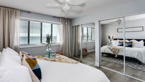 Un dormitorio moderno con una cama grande, un ventilador de techo y un ventanal corredera que da a otra habitación.
