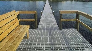 Un muelle de madera que se extiende hacia un frente marítimo con edificios al fondo.