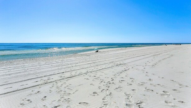 Una amplia playa de arena con huellas visibles y un cielo azul despejado.