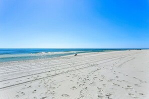 Une vaste plage de sable où l’on peut voir des empreintes de pas, et un ciel bleu dégagé.