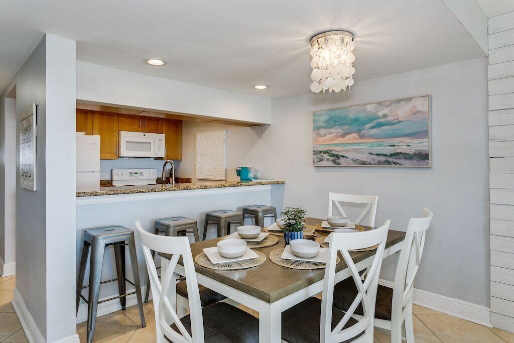 A modern kitchen with white cabinets, a microwave, and a dining area with white chairs and a table set for four.