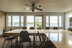 Una sala da pranzo con un grande tavolo in legno, sei sedie, una ventola a soffitto e ampie finestre che si affacciano sulle colline.