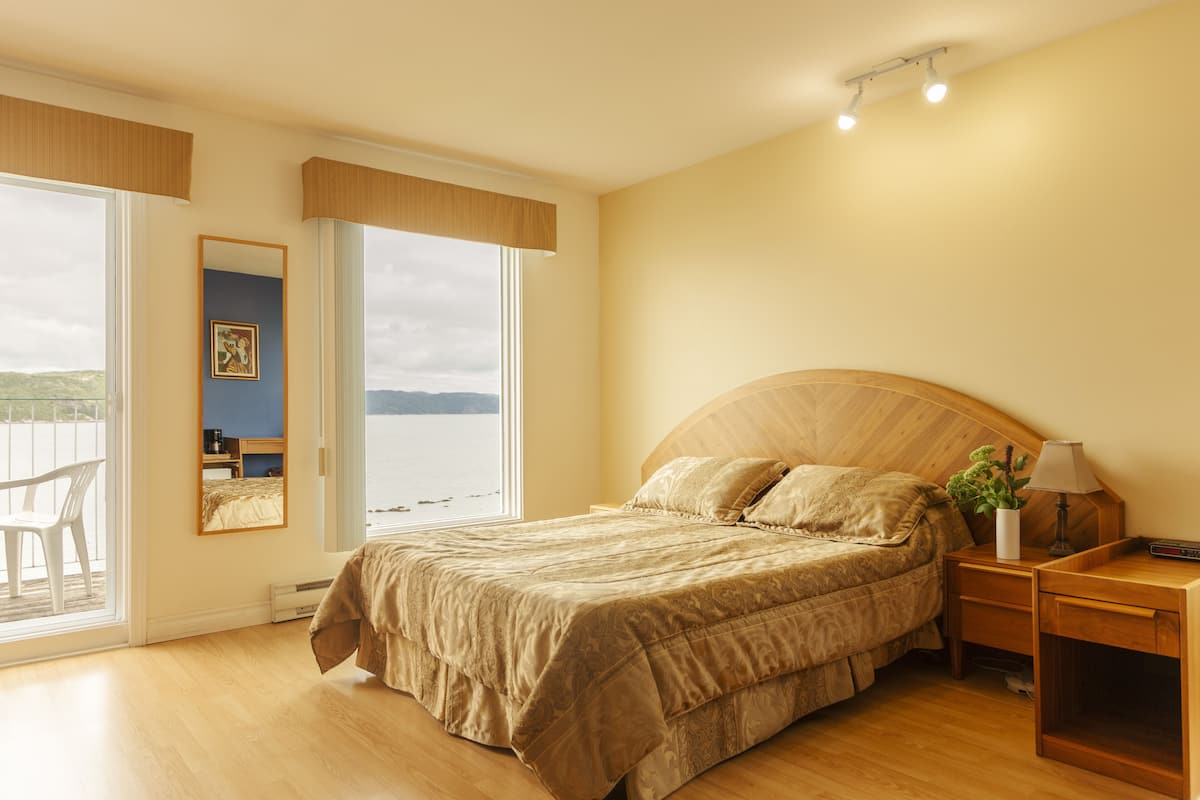 Ein Schlafzimmer mit einem großen Bett, einem Nachttisch, einem Spiegel und Blick ins Freie.