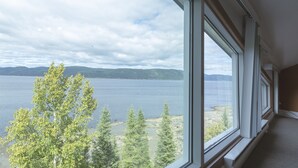Una habitación con ventanas amplias que dan a un lago y montañas a lo lejos.