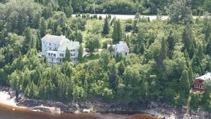 Un edificio blanco grande rodeado de un bosque frondoso, cerca de un cuerpo de agua.