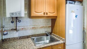 Una cocina compacta con armarios de madera, un lavamanos de acero inoxidable, un refrigerador blanco y un calentador de agua.