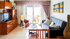 Una sala de estar con un sofá, televisor, aparador de madera, una silla y una mesa.