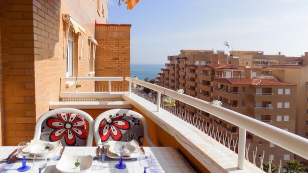 Un balcón con una mesa lista para comer, con vistas a la ciudad y al mar.