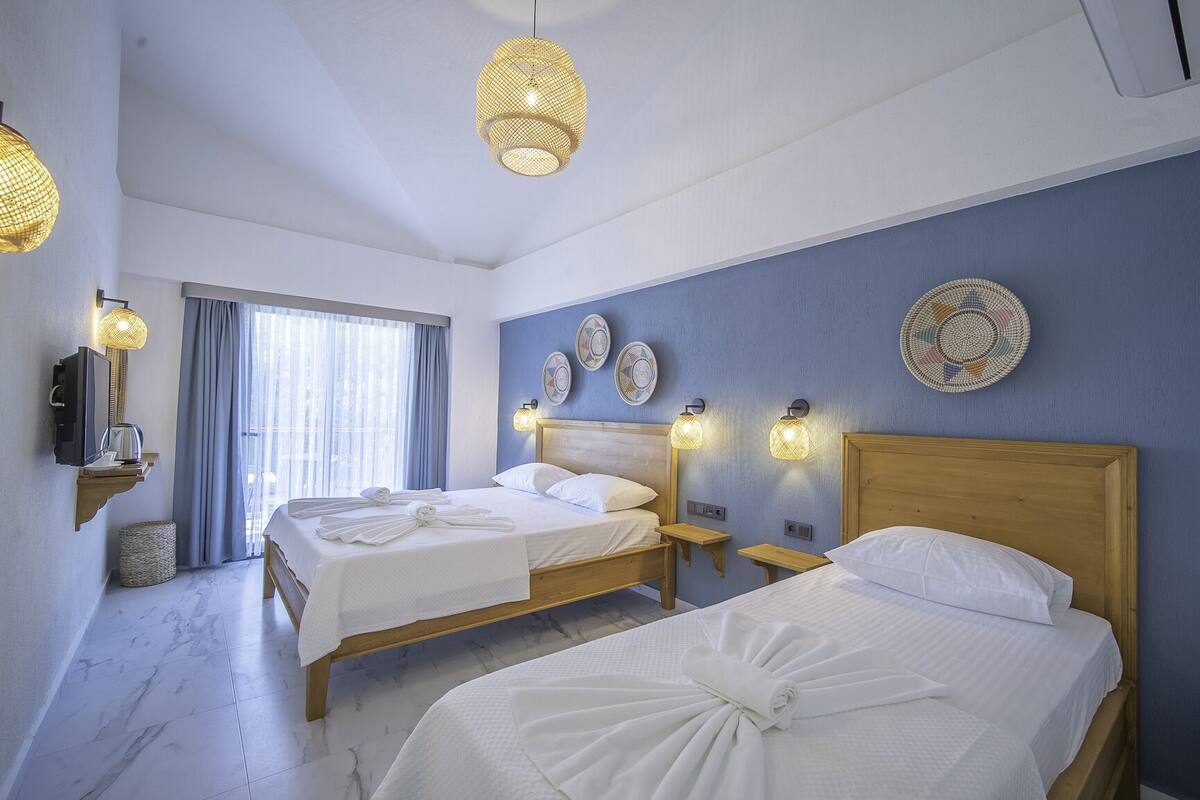 Ein Hotelzimmer mit zwei Betten, einem großen Fenster mit Vorhängen, einem Wandfernseher und dekorativen Wandplatten.