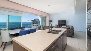 Eine moderne Küche mit einer großen Kochinsel, einem Essbereich mit blauen Stühlen und einem Fernseher an der Wand.