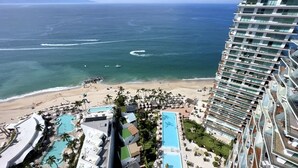 Ein Hochhaus-Hotel mit Blick auf den Strand, mehreren Schwimmbecken und einer Strandpromenade mit Palmen.